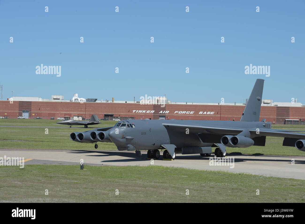 Two vital defense assets are shown together as a Boeing B-52H, 60-0005, poses in front of the  Oklahoma City Air Logistics Complex while a F-22A Raptor of the 325th Fighter Wing, Tyndall Air Force Base, Florida, rolls down the runway on May 1, 2017, Tinker Air Force Base, Oklahoma. OC-ALC is responsible for depot level maintenance of the B-52 fleet as well as overhaul of the Pratt & Whitney F119 engines used in the F-22A. (U.S. Air Force photo/Greg L. Davis) Stock Photo