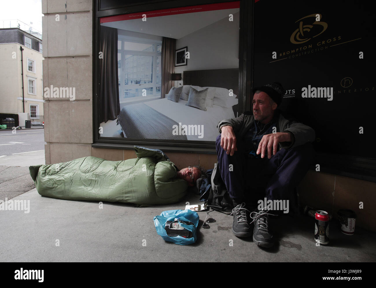 John and Chris sleeping rough next to a display advertising luxury apartments, in Victoria, London. Stock Photo