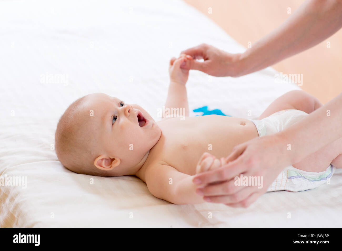 Mother or masseur massaging infant baby. Gymnastic, physical training, exercises for babies. Early development and health care concept. Stock Photo