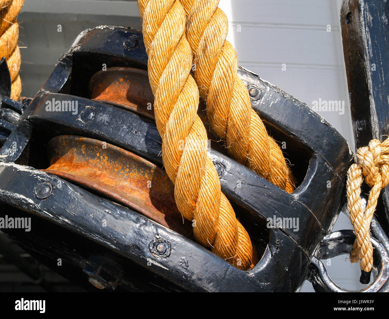 Old black double pulley with srtong rope closeup. Stock Photo