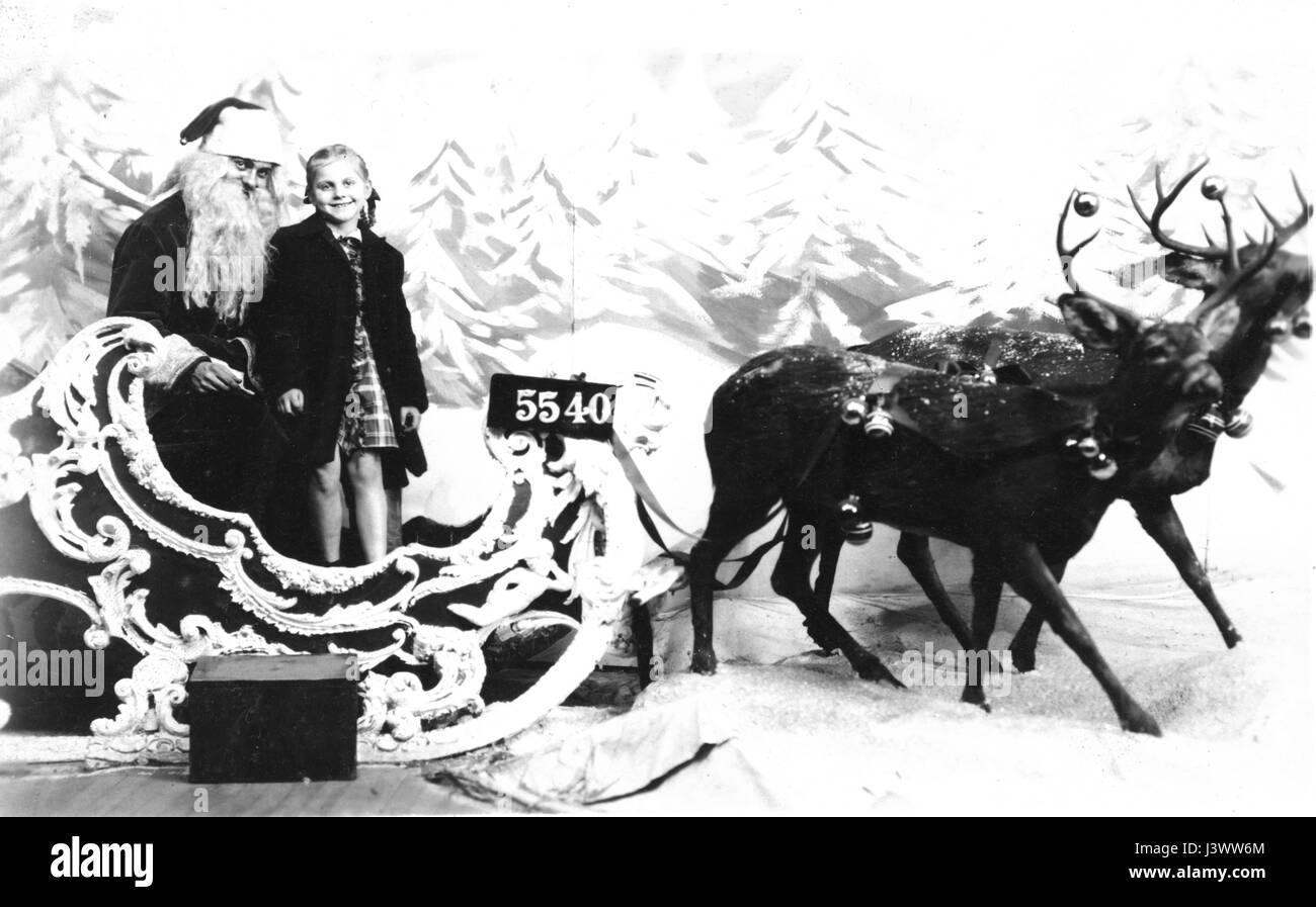 Department store Santa Clause (1930s), with a girl on his knee. Two Reindeer are 'pulling' a very ornate Santa sleigh. Both reindeer have Christmas ornaments hanging from their antlers.  Fake snow all around. This photo was number 5540 during that store's Christmas shopping season, and the photographer's box of all the necessary numbered cards is sitting right in front of the sleigh. To see my other Christmas-related vintage images, Search:  Prestor  vintage  holiday  [or vehicle] Stock Photo