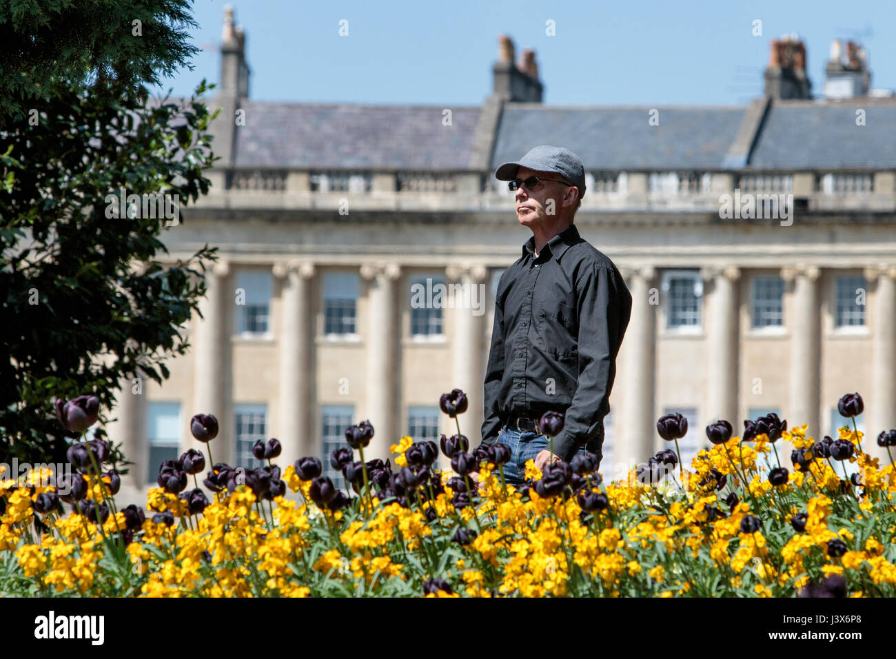 Bath, UK. 8th May, 2017. UK Weather. With the world famous Royal Crescent in the background, a man enjoying the warm sunshine is pictured as he walks past colourful flower displays in Royal Victoria park. Credit: lynchpics/Alamy Live News Stock Photo