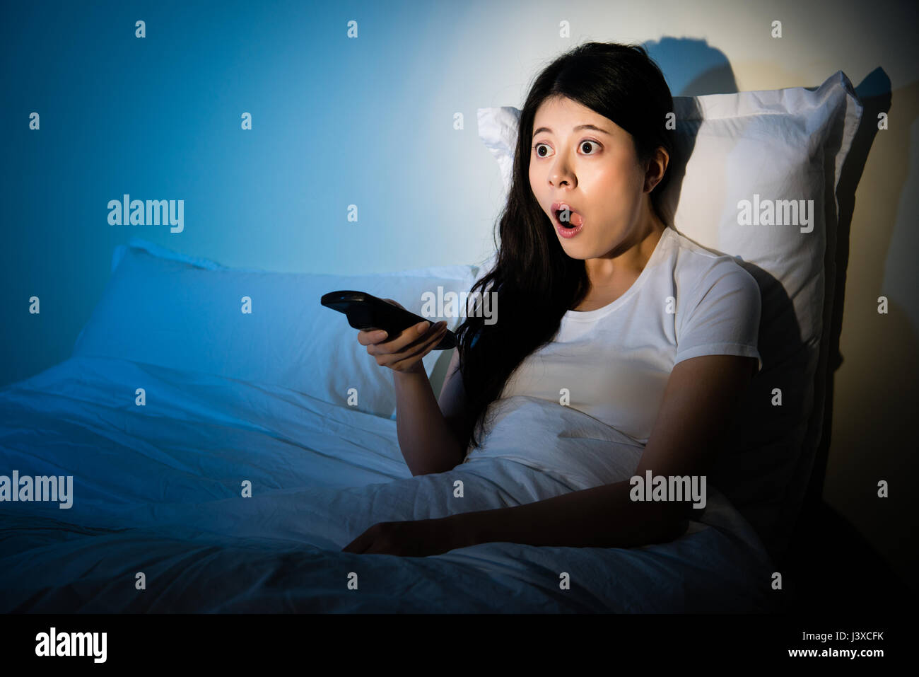 Portrait of young girl sitting on sofa watching a movie with shocked expression on faces. mixed race asian chinese model. Stock Photo
