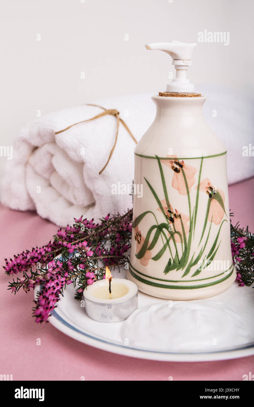 Lotion in an attractive pottery container, surrounded by heather (Erica darleyensis), a tea candle and a bath towel Stock Photo