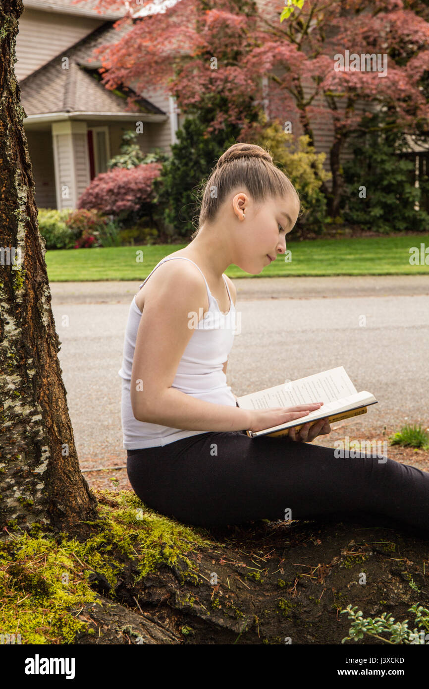 Eleven year old girl reading a book in the shade of a tree in Issaquah