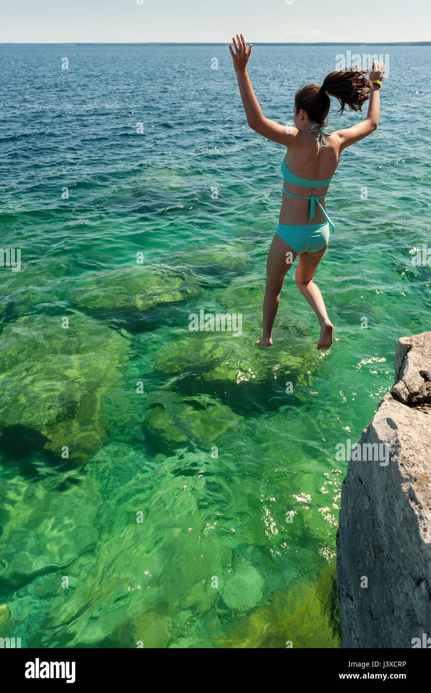 Summer, 16-19 year old teenager girl jumping in a lake from a cliff at Bruce Peninsula, Fathom Five National Marine Park, Tobermory, Ontario, Canada. Stock Photo