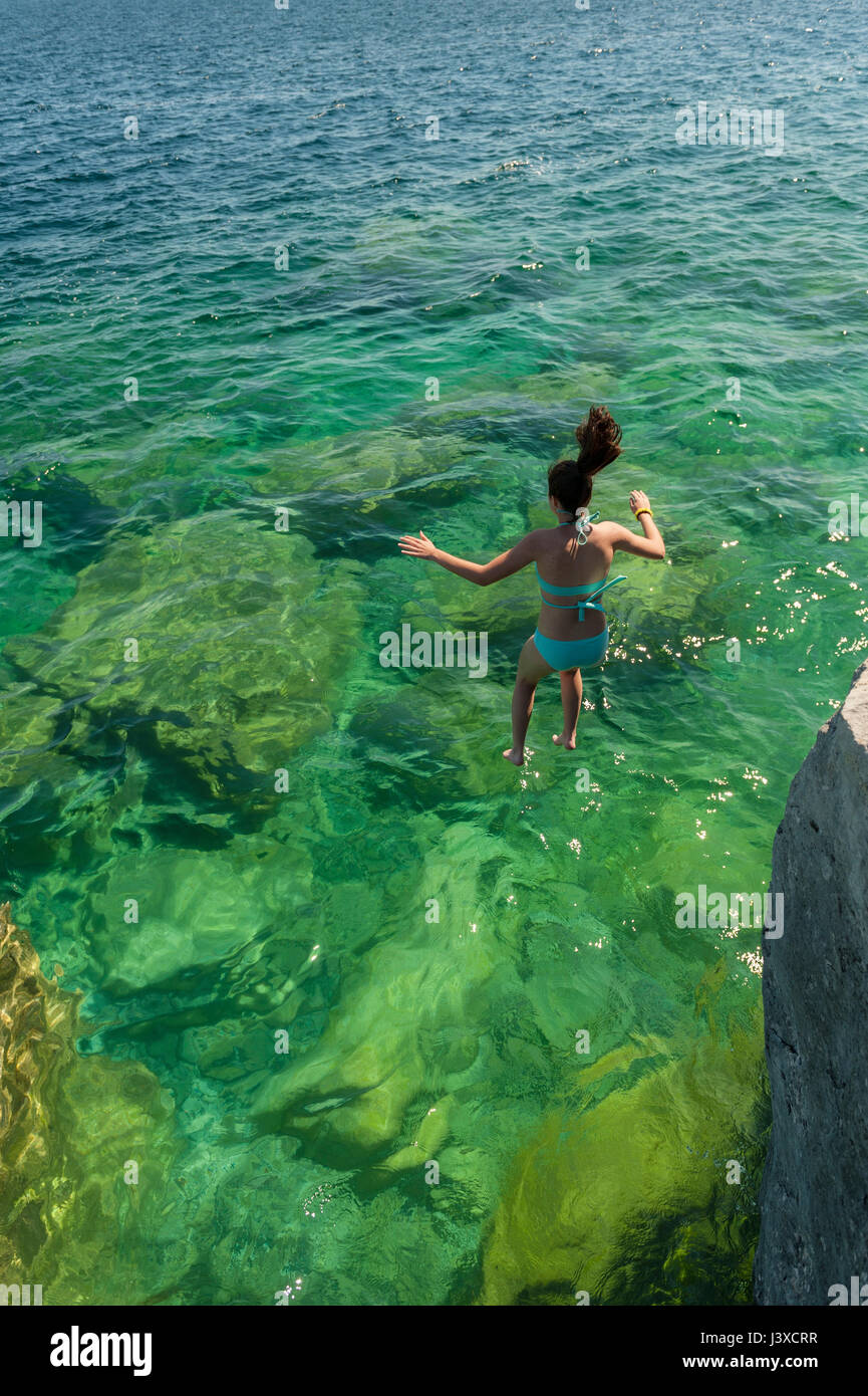Summer, 16-19 year old teenager girl jumping in a lake from a cliff at Bruce Peninsula, Fathom Five National Marine Park, Tobermory, Ontario, Canada. Stock Photo