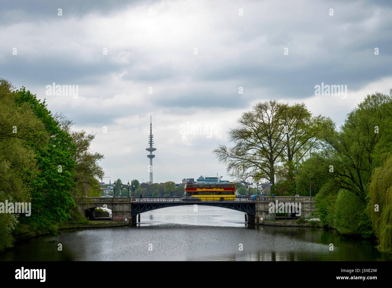 The city of Hamburg: view to moving people, to a moving red-yellow tourist bus, the television tower and the Alster, Germany Stock Photo