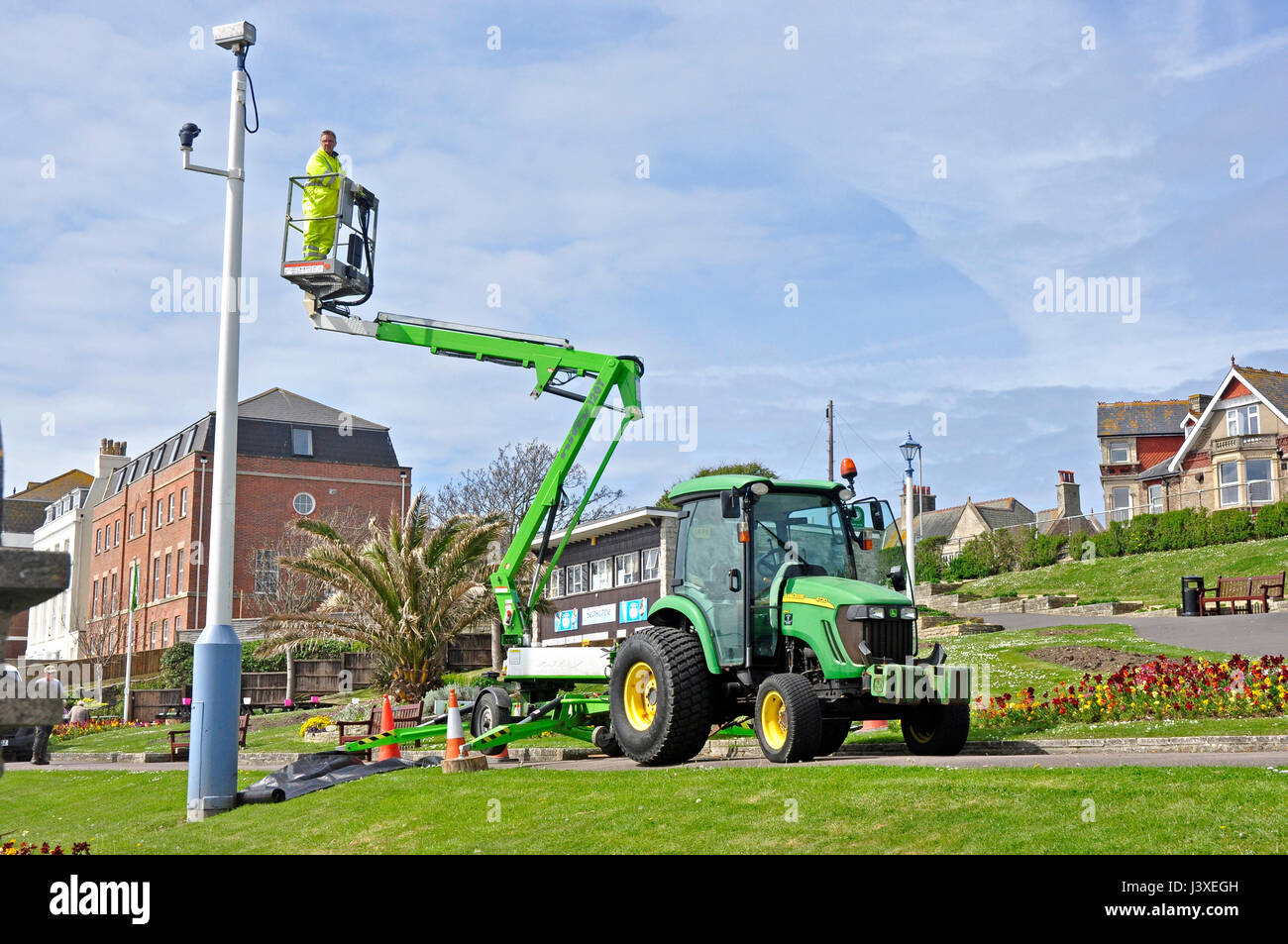 Workman inspecting high level CCTV  using articulated tub lift mounted on tractor + trailer - seafront pleasure gardens - ready for the tourist season Stock Photo