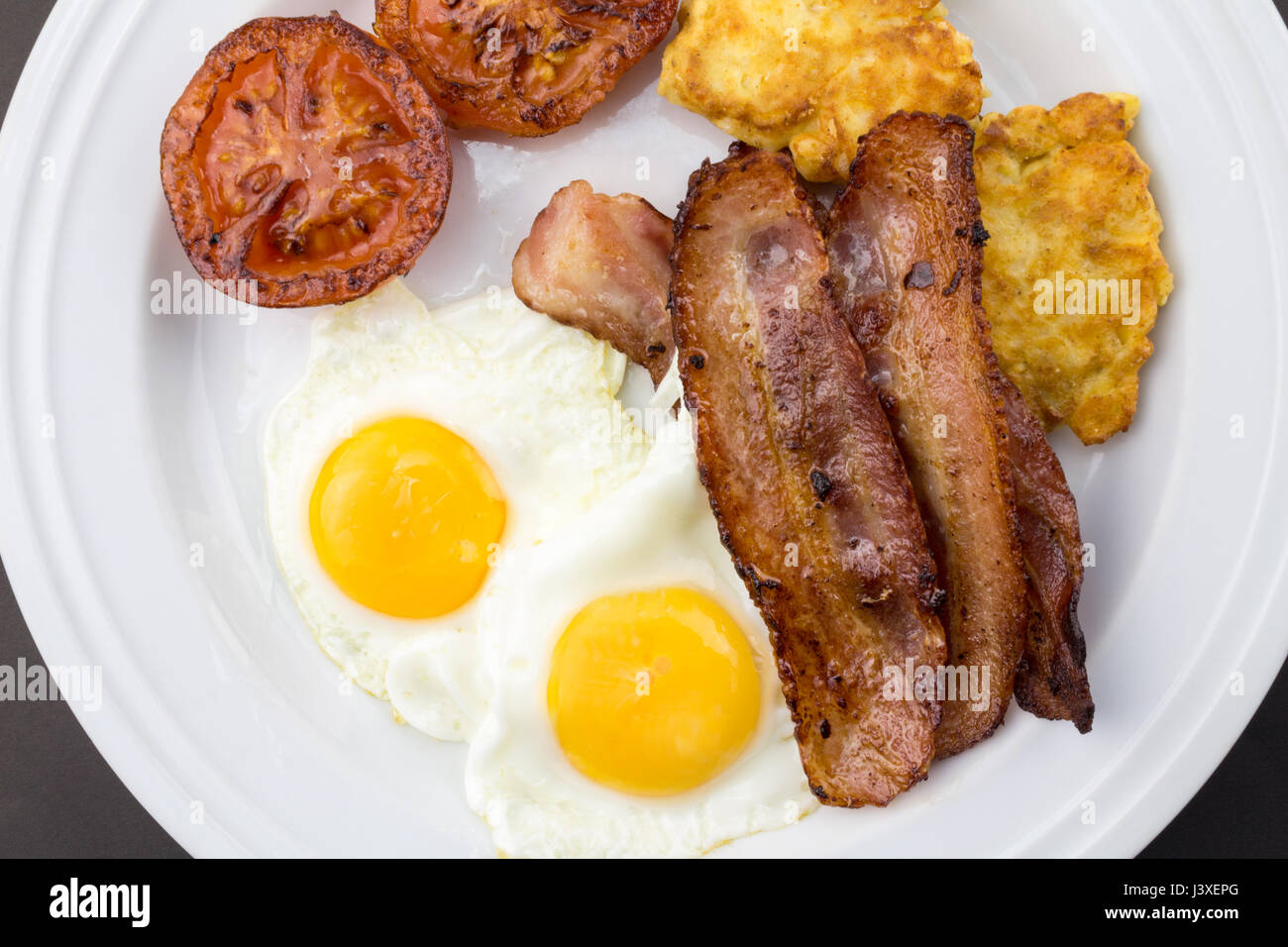 Breakfast with fried eggs, bacon, tomato and potato griddle cakes close