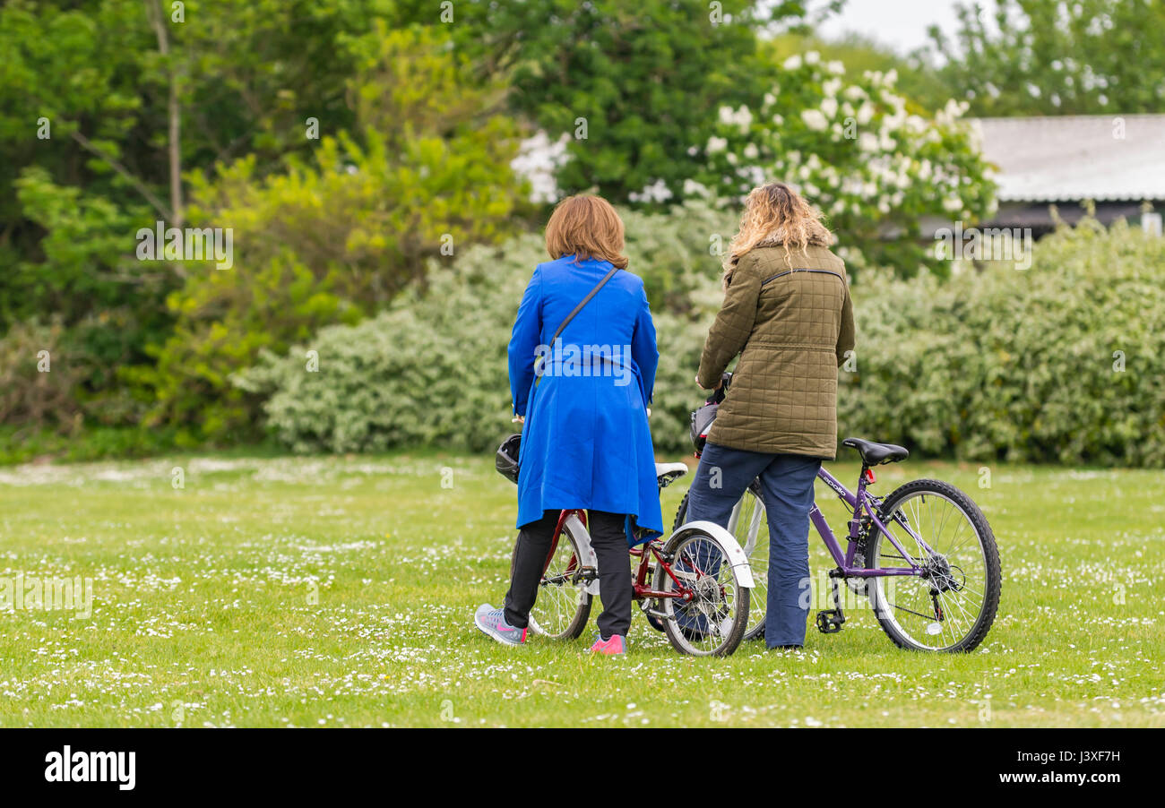 Pair of women pushing bicycles on grass through a park. Stock Photo