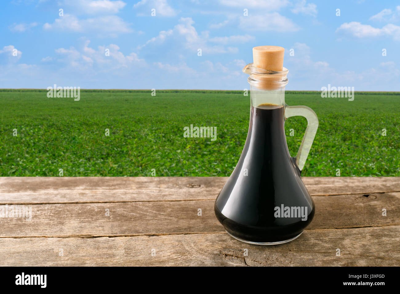soy sauce in glass bottle on wooden table with green field on the background. Soybean field with blue sky. Photo with copy space area for a text. Seas Stock Photo