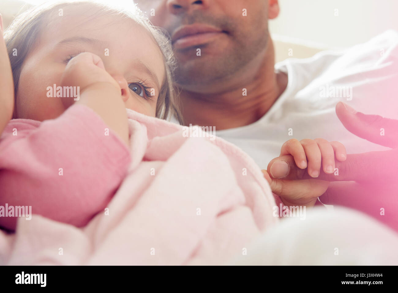 Baby girl sucking thumb with comfort blanket on father's lap Stock Photo
