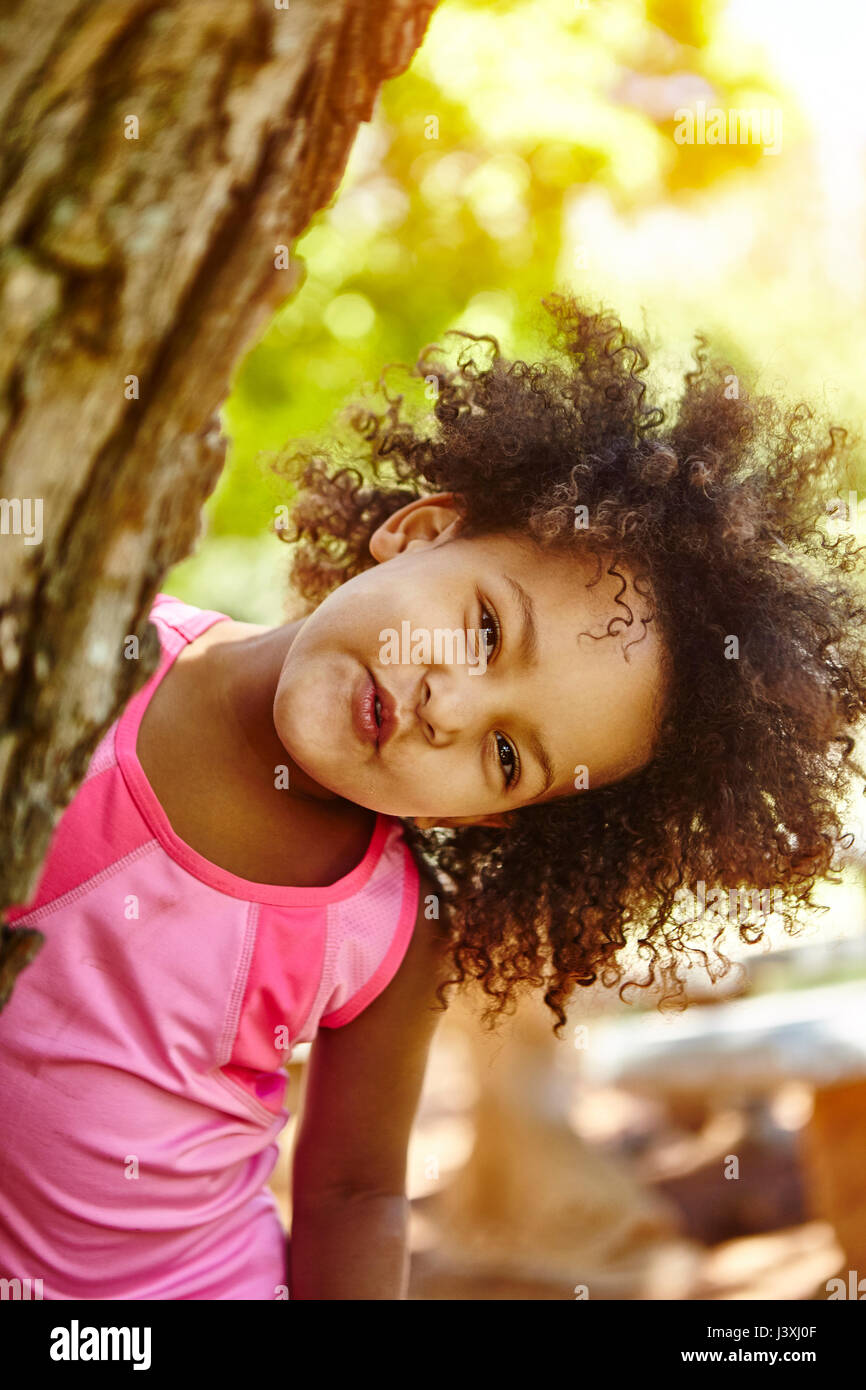Portrait of young girl, peering out from behind tree, smiling Stock Photo