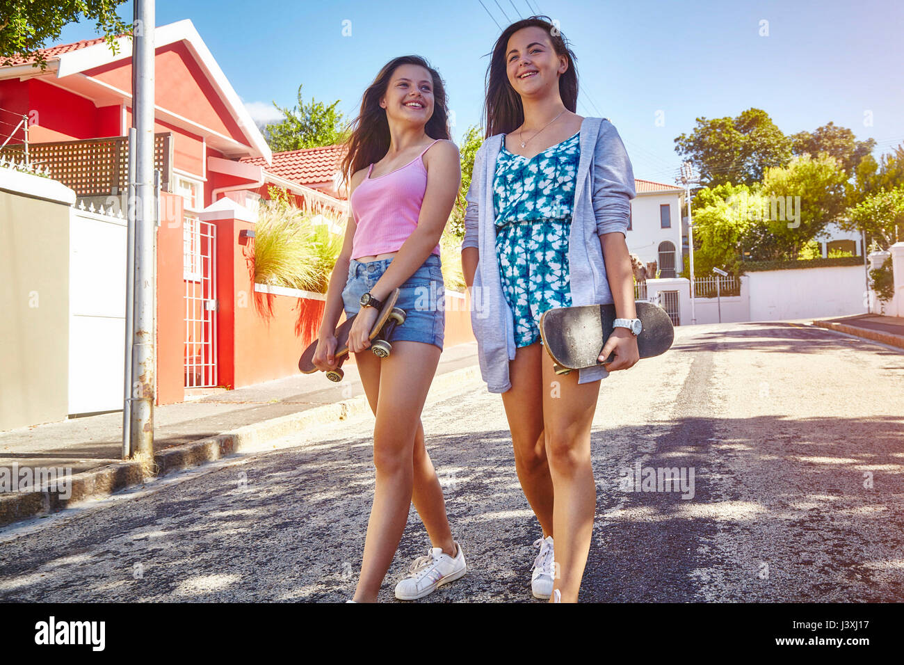 Two female friends, walking outdoors, carrying skateboards Stock Photo