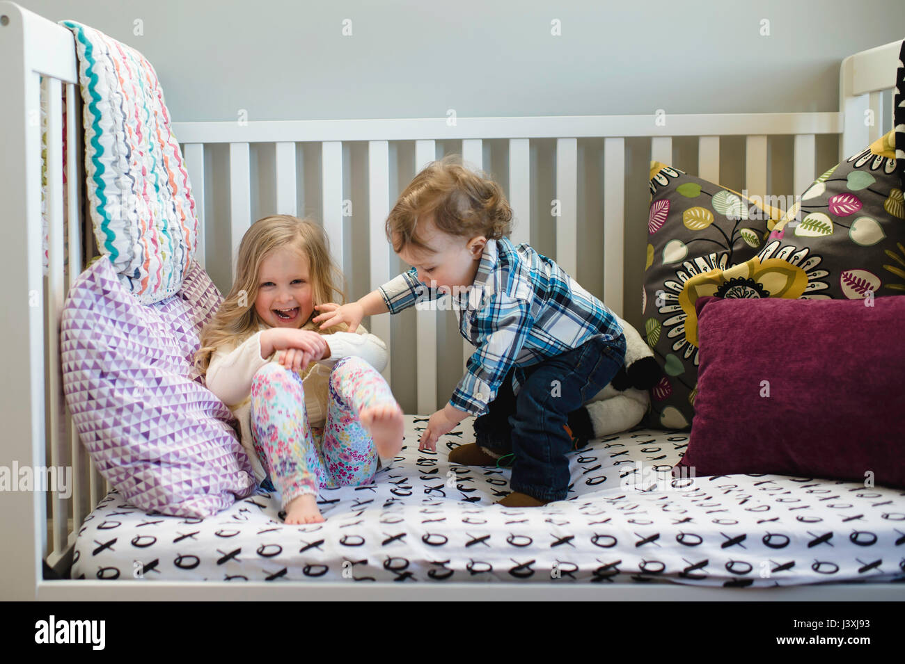 Male toddler and sister playing on day bed Stock Photo