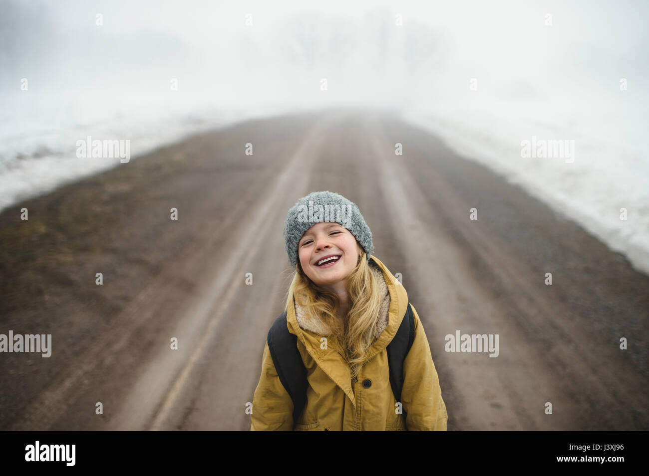 Portrait of girl in knit hat standing in middle of foggy dirt road laughing Stock Photo