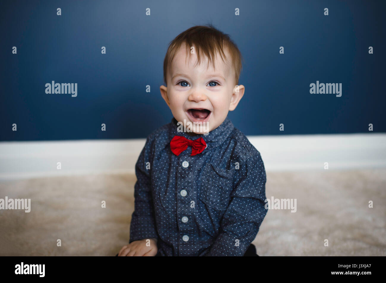 Portrait of male toddler in red bow tie sitting on floor Stock Photo