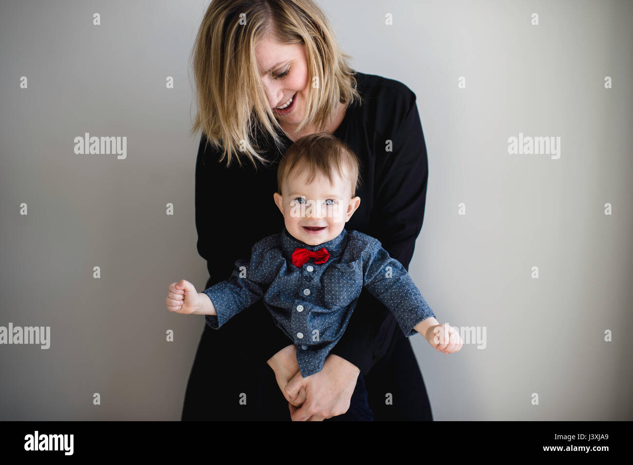 Portrait of male toddler in red bow tie being held by mother Stock Photo