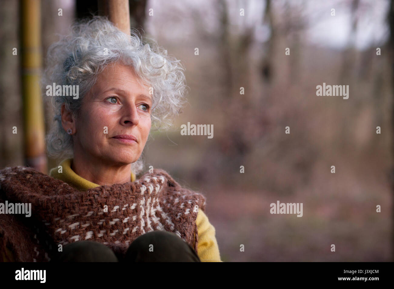 Portrait of grey haired mature woman gazing in woodland at dusk Stock Photo