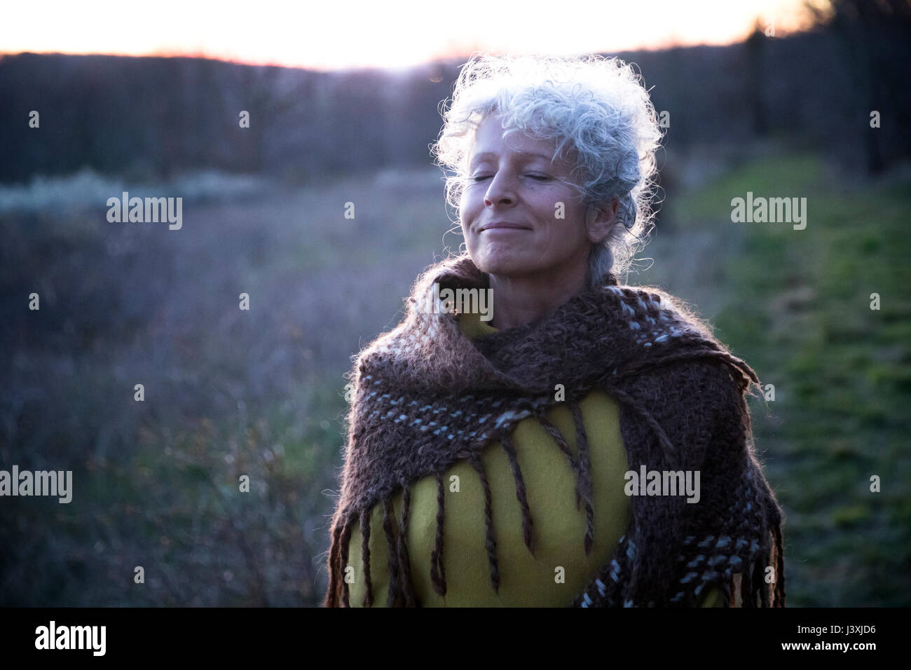 Portrait of mature grey haired woman with eyes closed in dusk landscape Stock Photo