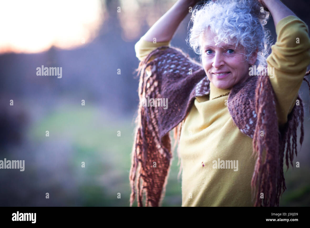 Portrait of mature woman with hands in grey hair in dusk landscape Stock Photo