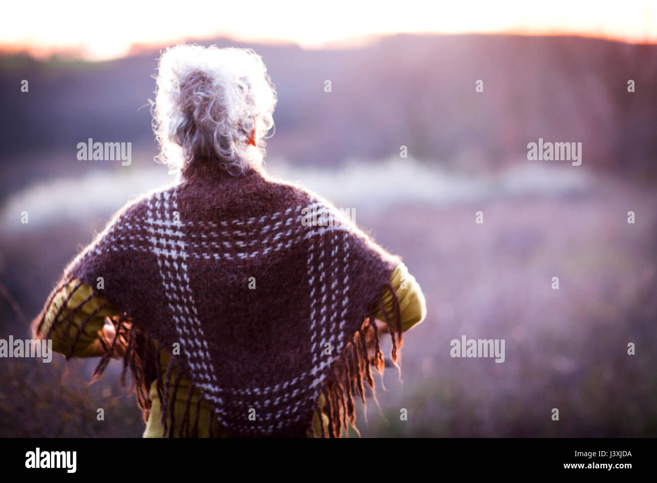 Rear view of mature woman watching sunset over rural landscape Stock Photo