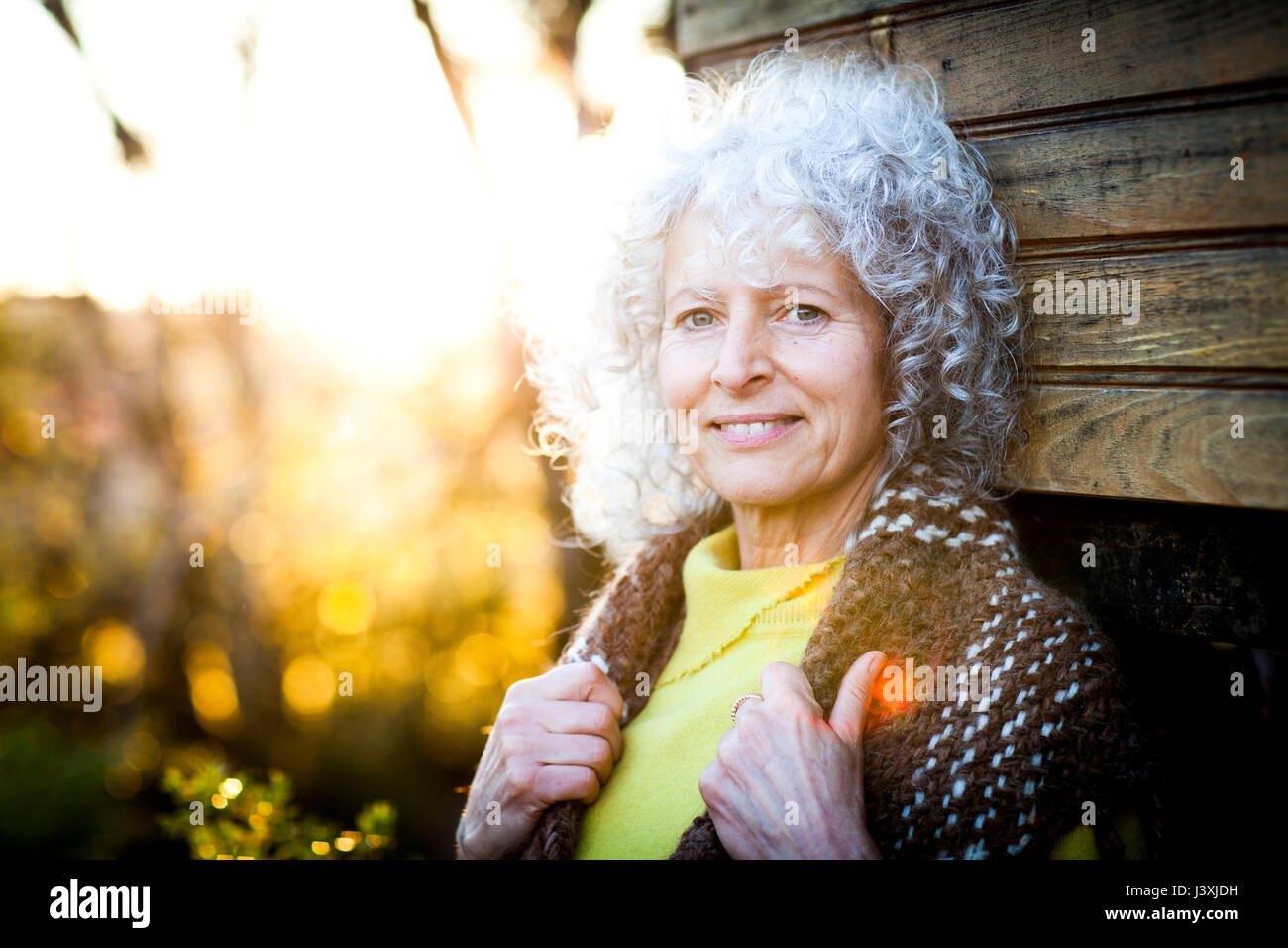 Portrait of mature woman with grey hair leaning against woodland treehouse at sunset Stock Photo