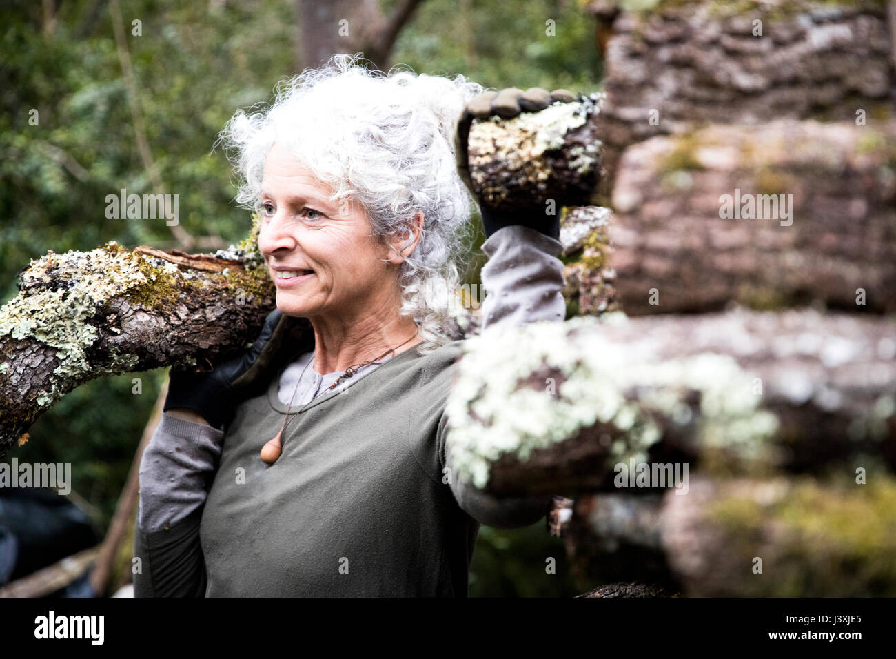 Mature woman carrying log on her shoulder in garden Stock Photo