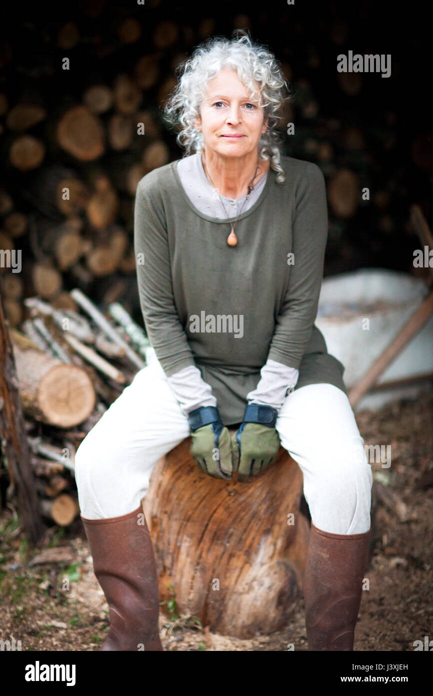 Portrait of mature grey haired woman sitting on log in garden Stock Photo