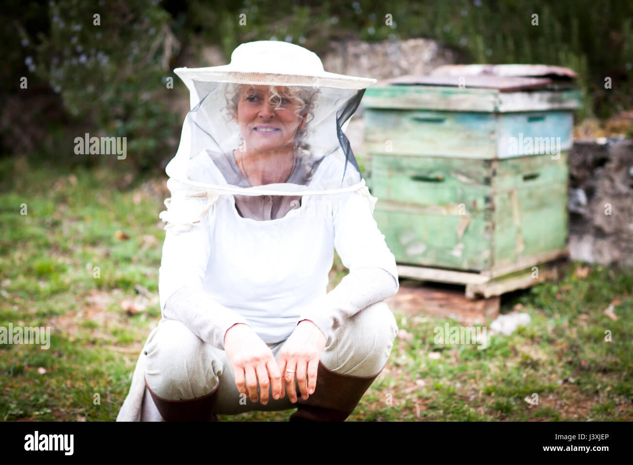 Portrait of female beekeeper crouching in garden Stock Photo