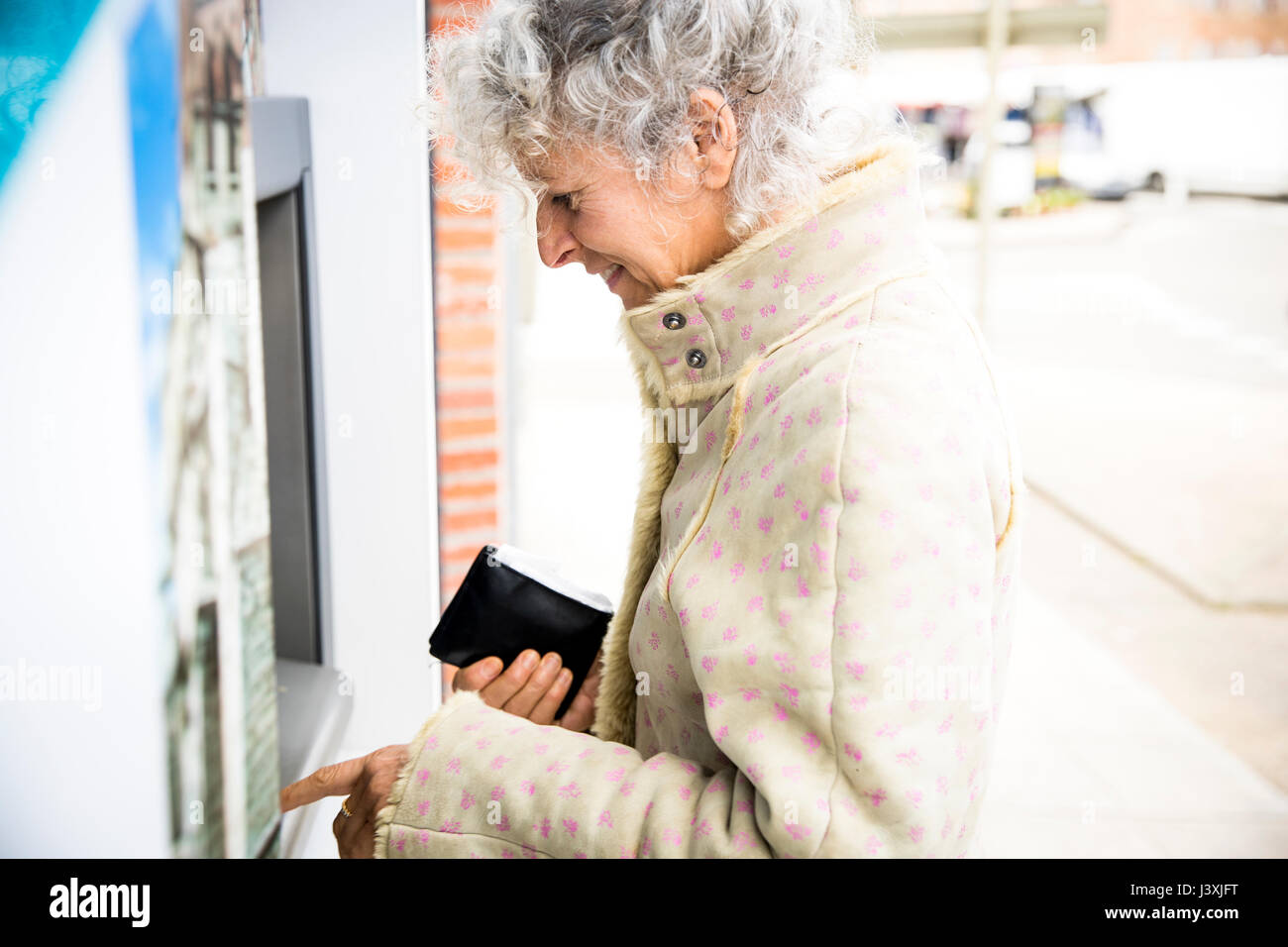 Mature woman pressing PIN at local french cash machine Stock Photo