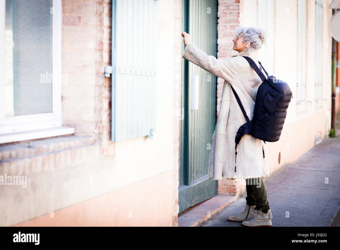 Mature woman pressing front door bell in local french village Stock Photo