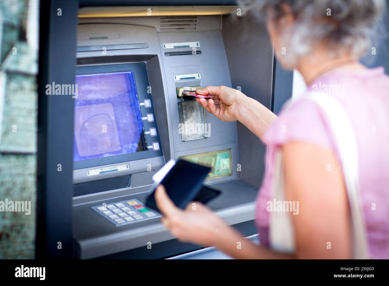 Mature woman inserting credit card into local french cash machine Stock Photo