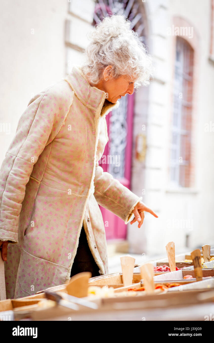 Mature female shopper buying dried food at local french market Stock Photo