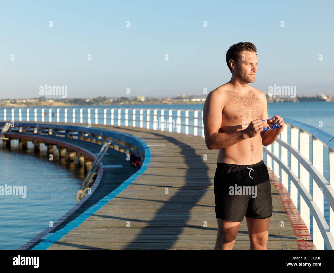 Swimmer holding swimming goggles on boardwalk, Eastern Beach, Geelong, Victoria, Australia Stock Photo