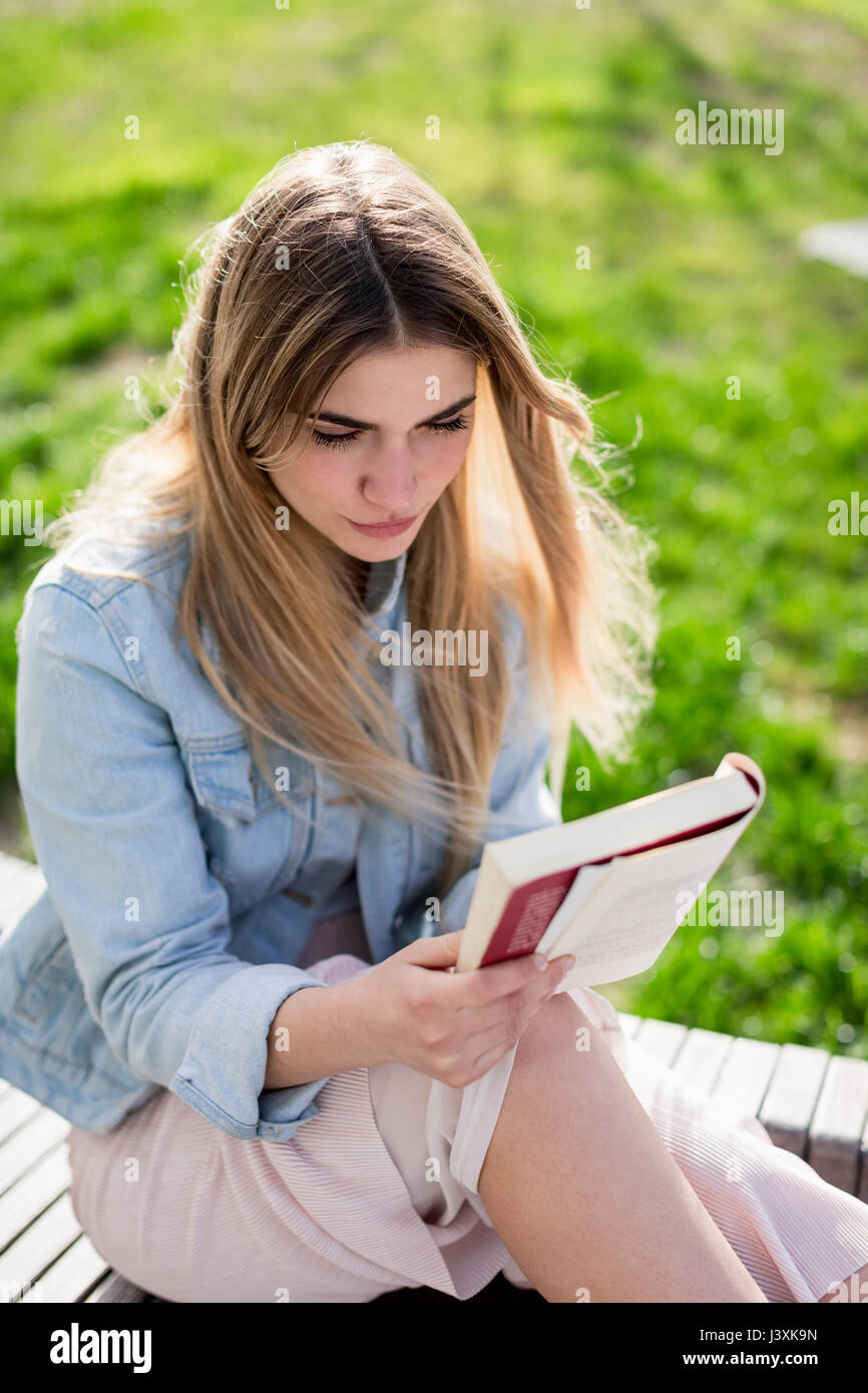Young woman sitting outdoors, reading book Stock Photo - Alamy