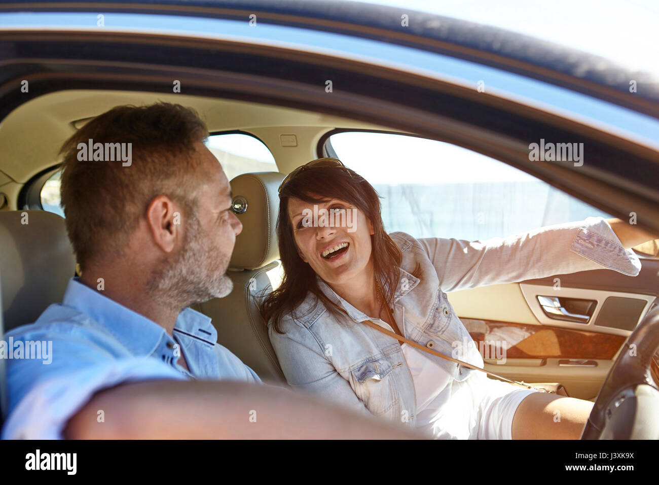 Couple in car, man driving, woman pointing ahead, laughing Stock Photo