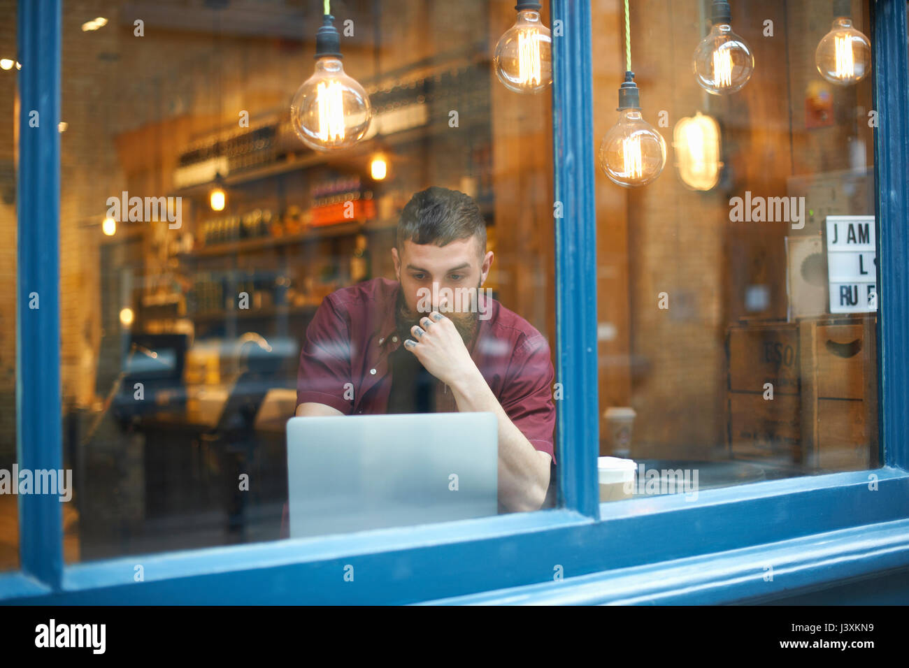 Window view of young man using laptop in cafe Stock Photo