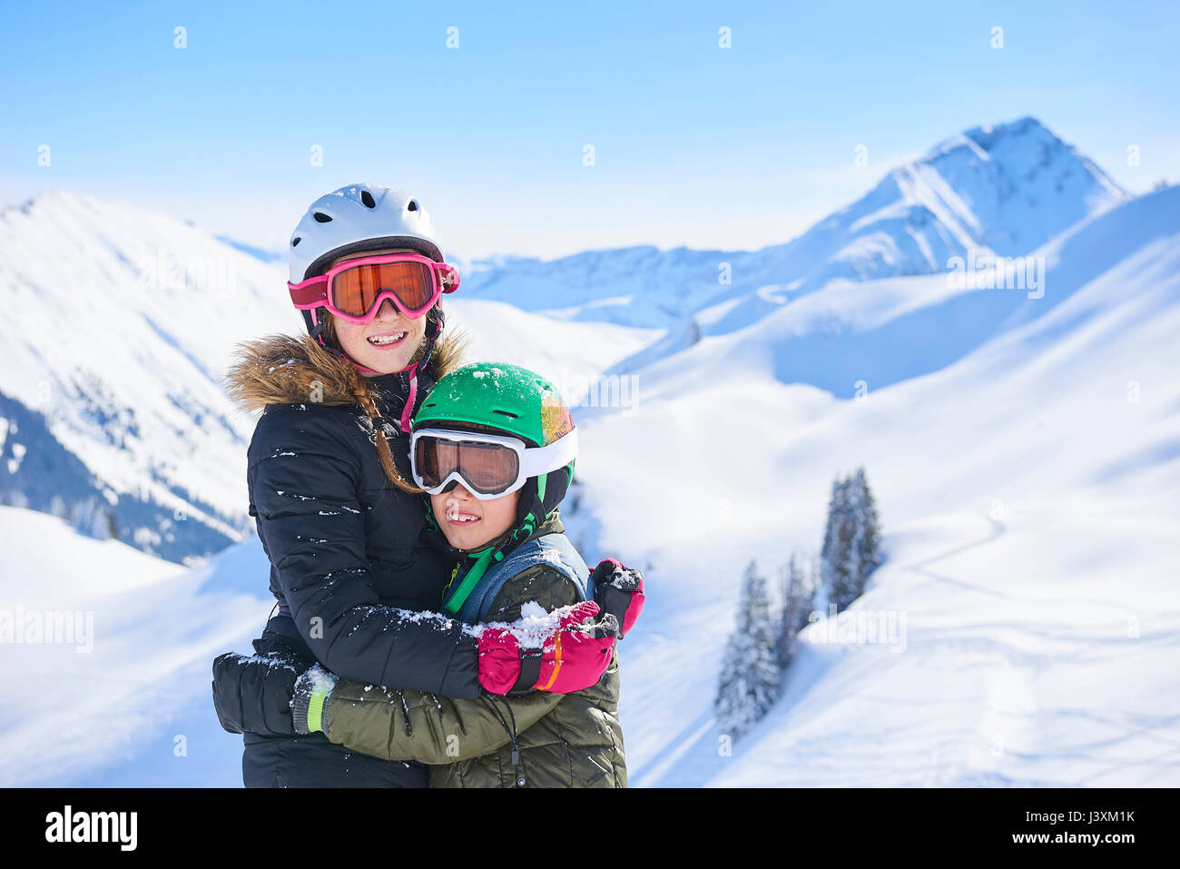 Portrait of skiing teenage girl and brother hugging in Swiss Alps