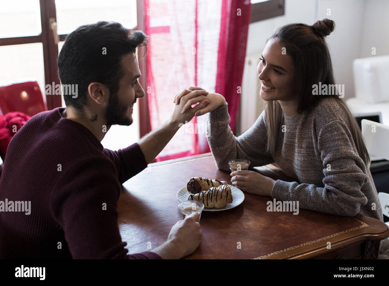 Couple sitting at table holding hands, drinking coffee Stock Photo