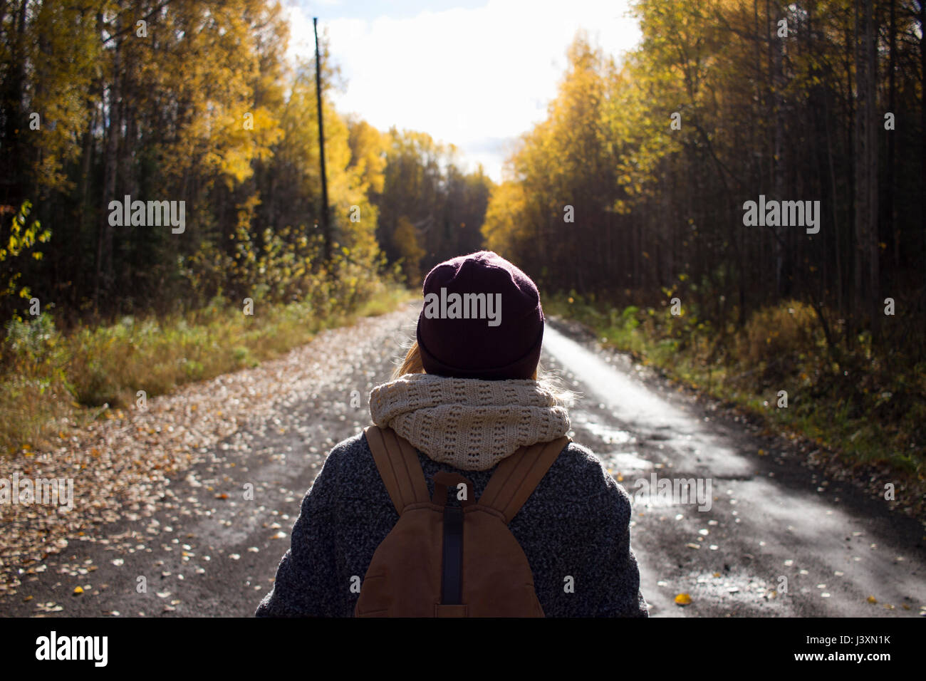 Young woman hiking, on empty country road, rear view, Sverdlovsk Oblast, Russia Stock Photo