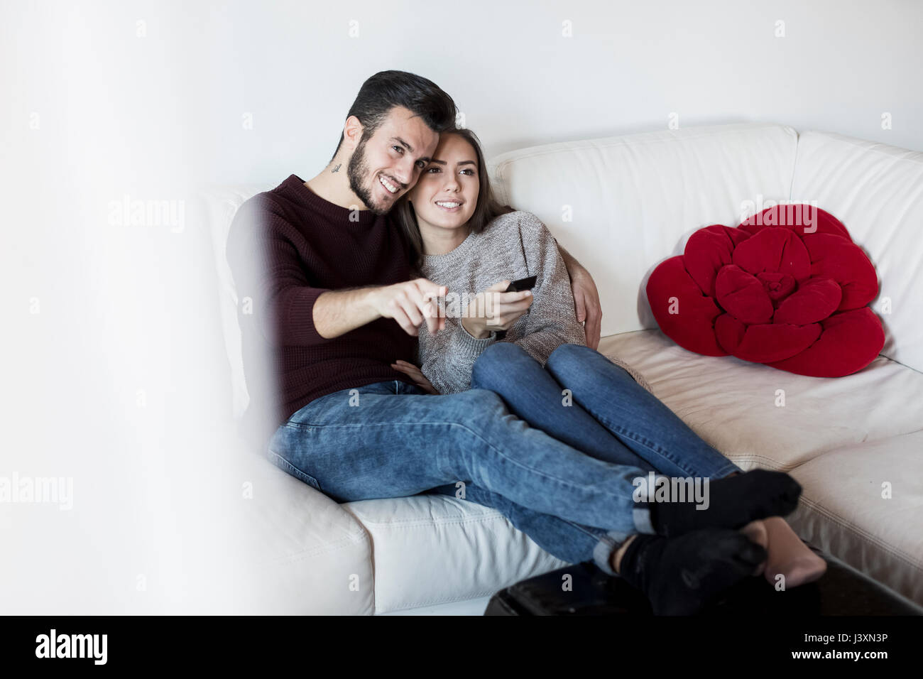 Young couple relaxing on sofa, watching TV, young woman holding remote control Stock Photo