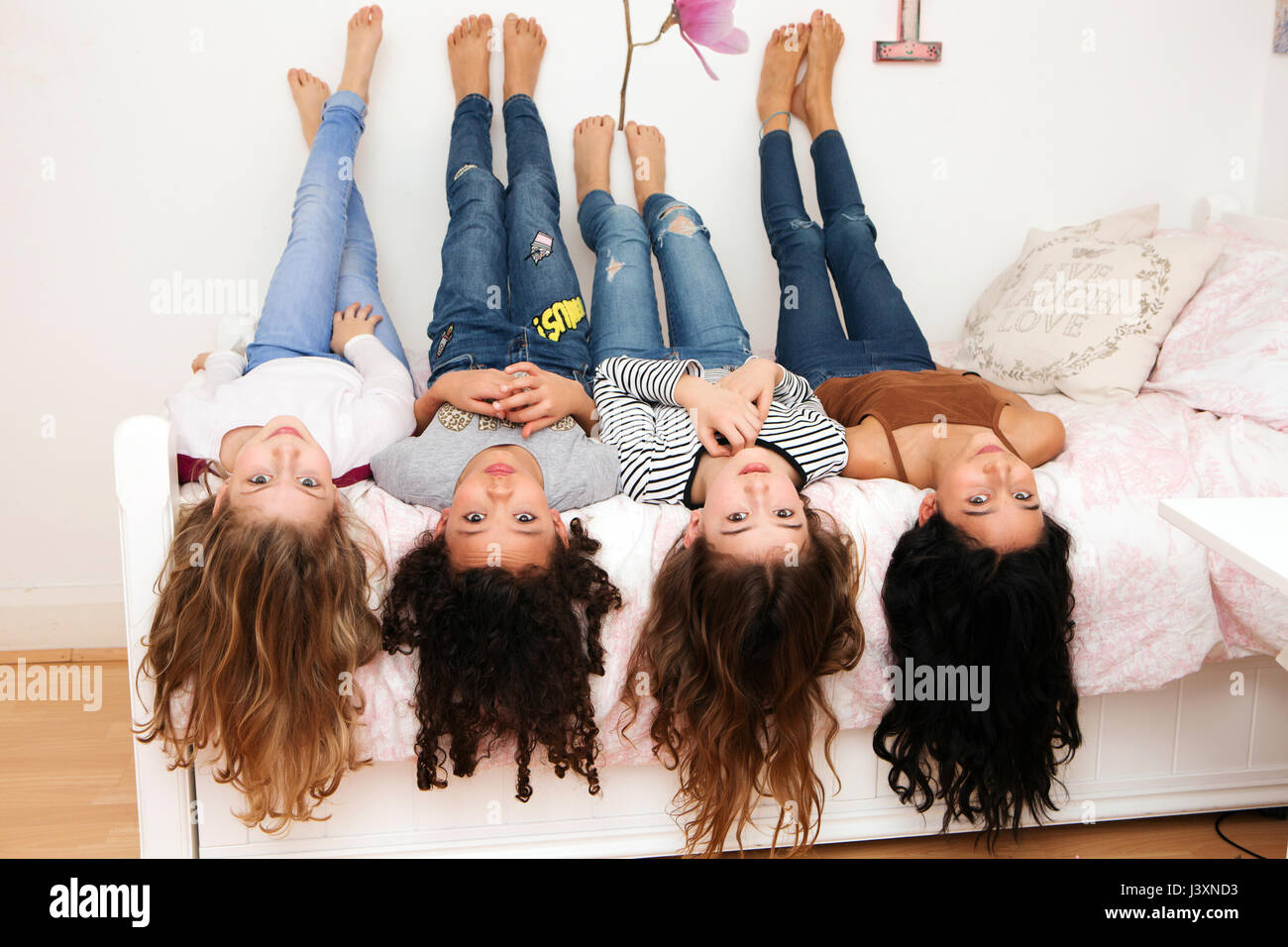 Girls lying upside down on bed looking at camera Stock Photo