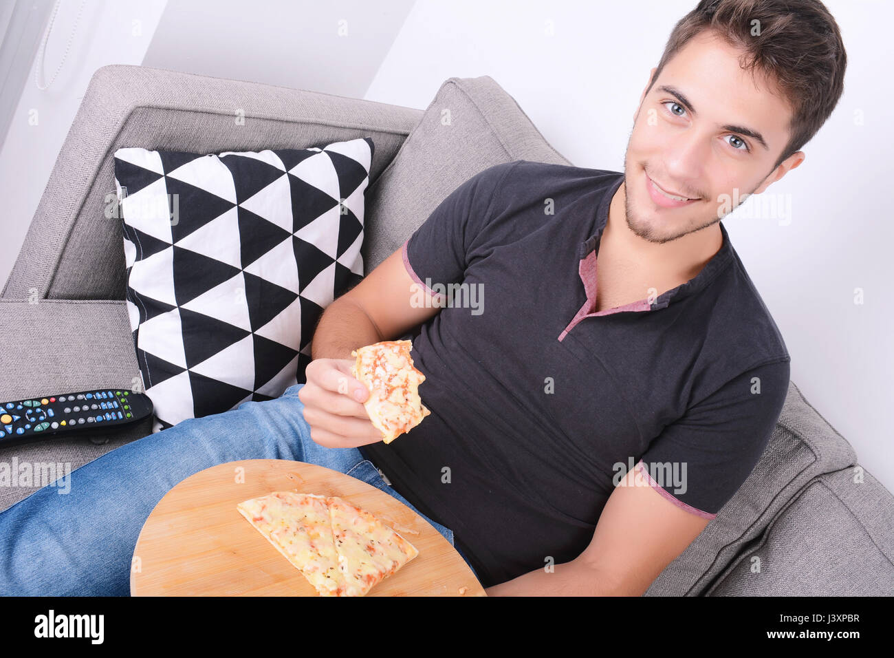 Attractive young man eating pizza on couch. Indoors. Stock Photo