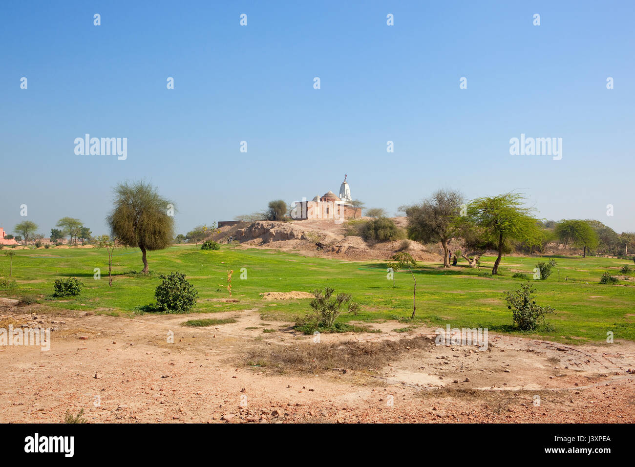a hindu temple at the top of bhatner fort hanumangarh rajasthan india with grass acacia trees and restoration work under a clear blue sky in springtim Stock Photo