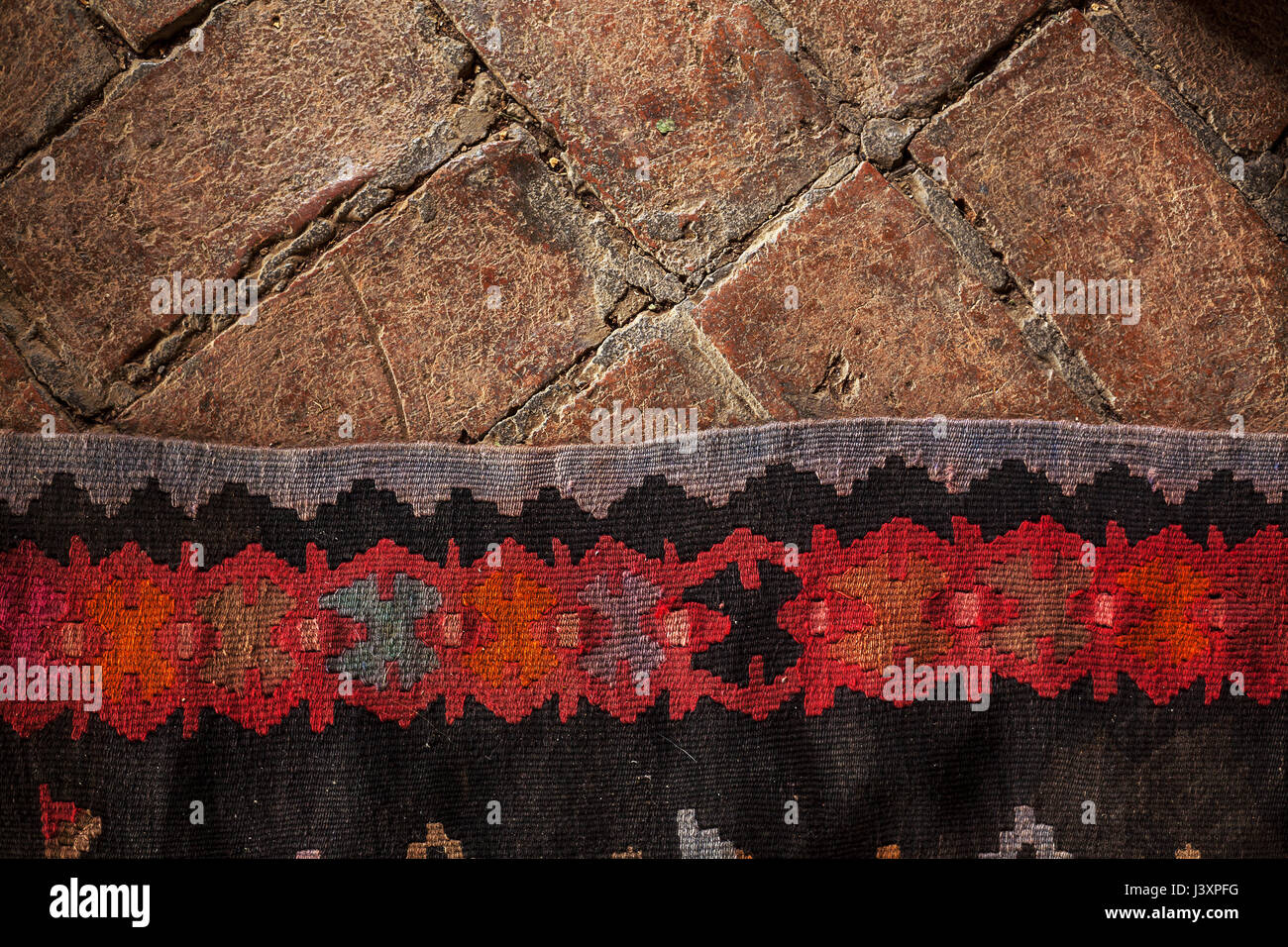 Details of an old decorative embroidery carpet on brick floor. Stock Photo