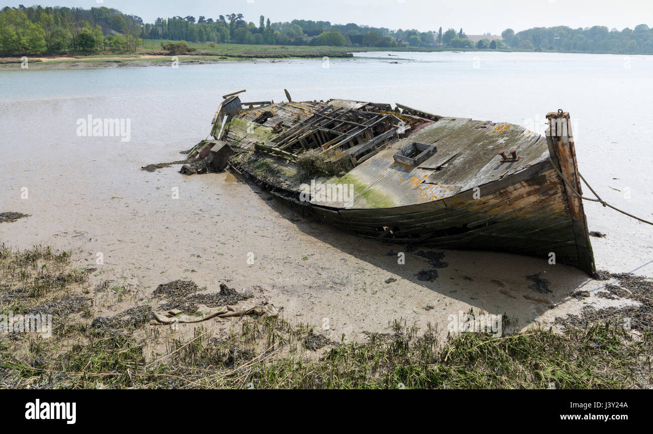 Derelict and rotting wooden boat have submerged in silt at low tide on