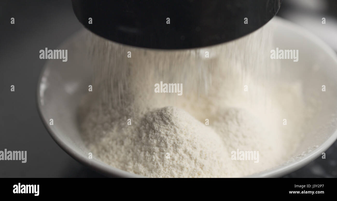 Handheld shot of sieving flour with mug sieve on plate closeup Stock