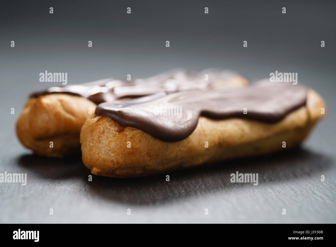 two eclairs with dark chocolate on top on slate background Stock Photo